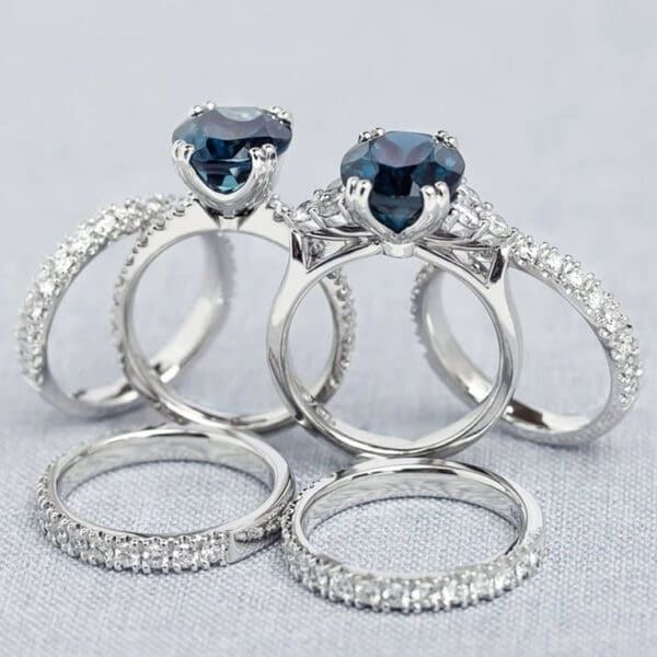 Pair of teal sapphire engagement rings with matching diamond wedding rings.