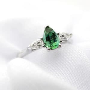 Pear trio engagement ring featuring a bright green sapphire and diamonds in a white gold setting