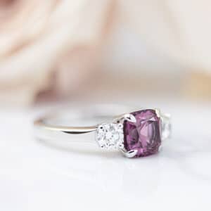 Three stone engagement ring design with a purple sapphire and two accent diamonds in white gold.