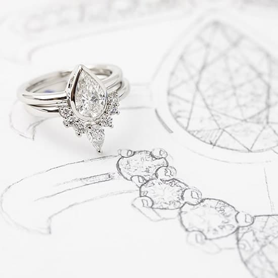 Custom made wedding ring custom fitted to engagement ring resting on jewellery design sketches.