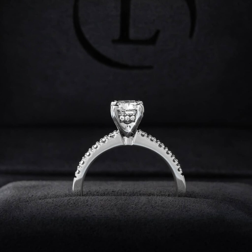 The profile of an engagement ring with a diamond-encrusted band, solitaire centre stone and a band of diamonds underneath the main stone, called a hidden halo.