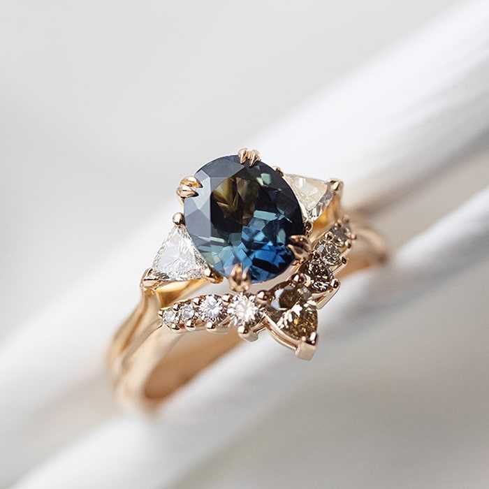 Close up of bespoke sapphire engagement ring paired with a diamond wedding ring