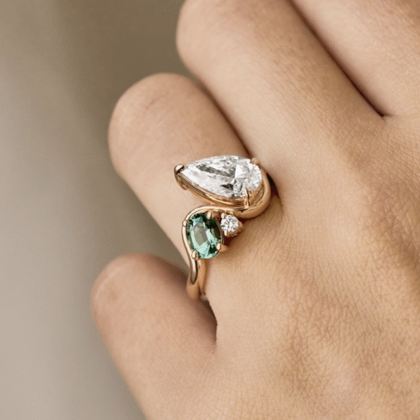 Green Oval Cut Gemstone Paired with a Pear Shaped Diamond Positioned in a Ribbon Band